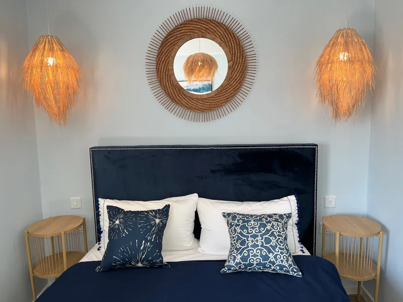 Double bedroom with a navy velvet headboard, rattan mirror and woven pendant lights
