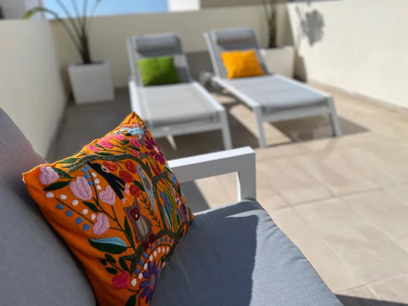 Embroidered cushion on a back terrace sofa with sun loungers behind